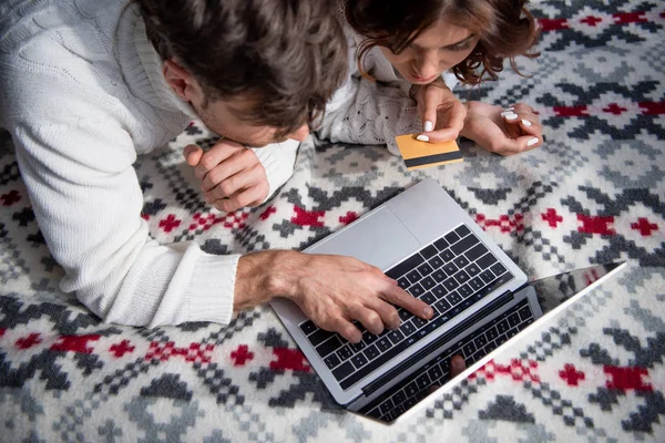 Высокий угол зрения бойфренда, указывающего пальцем на ноутбук и подругу, держащую кредитную карту — стоковое фото