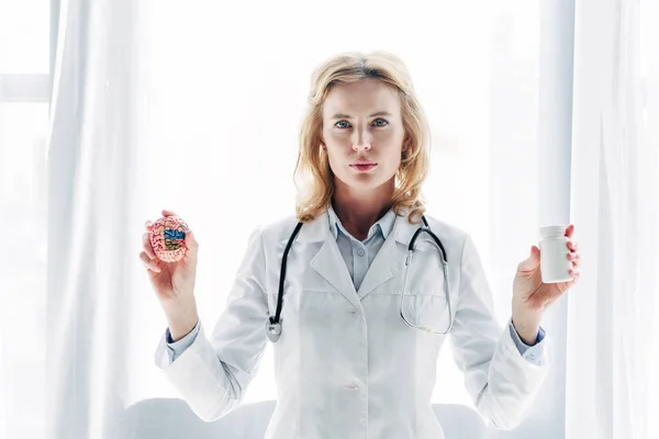 Doctor in white coat holding model of brain and bottle with pills in clinic — Stock Photo