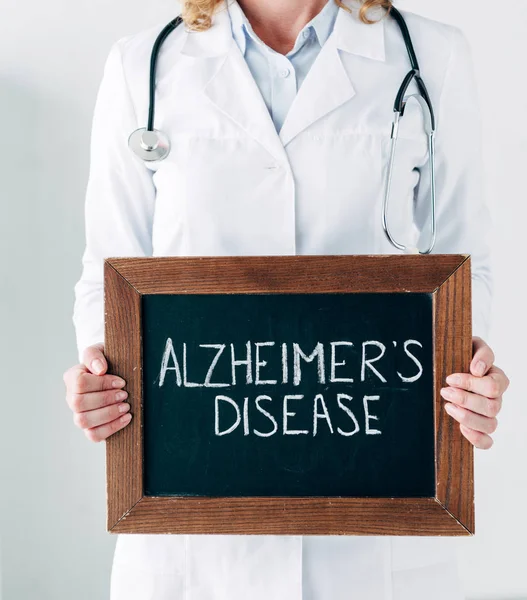 Vue recadrée du médecin en manteau blanc tenant une planche de bois avec lettrage maladie d'Alzheimer — Photo de stock