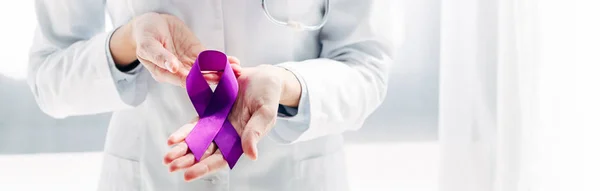 Panoramic shot of doctor in white coat holding purple ribbon in clinic — Stock Photo
