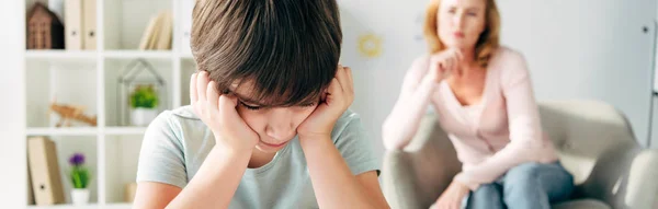Panoramic shot of sad kid with dyslexia and child psychologist on background — Stock Photo
