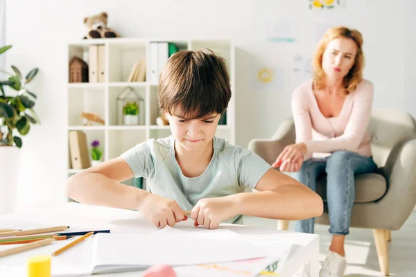 Messa a fuoco selettiva del bambino arrabbiato con dislessia rottura matita e psicologo infantile su sfondo — Foto stock