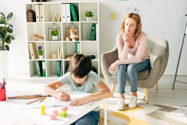 Kind mit Legasthenie malt mit Bleistift und Kinderpsychologe schaut ihn an — Stockfoto