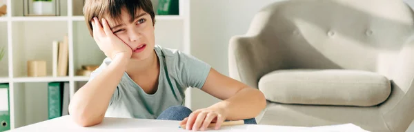 Plano panorámico de niño pensativo con dislexia sentado a la mesa - foto de stock