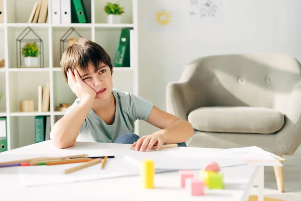 Niño pensativo con dislexia sentado en la mesa y mirando hacia otro lado - foto de stock