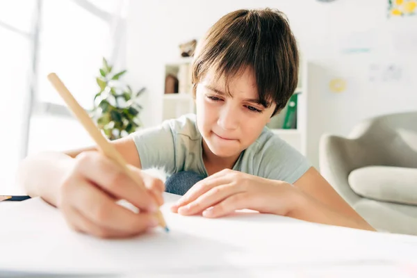 Enfant avec dyslexie dessin au crayon et assis à la table — Photo de stock