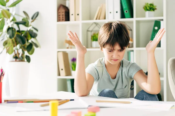 Niño irritado con dislexia sentado en la mesa y mirando hacia abajo - foto de stock