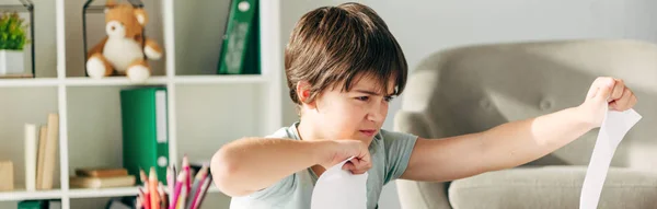 Panoramic shot of irritated kid with dyslexia punching paper — Stock Photo