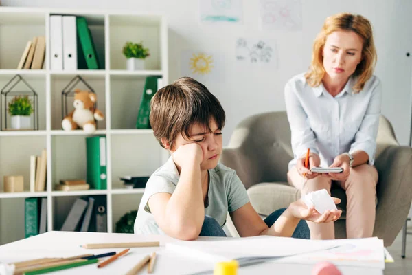 Selective focus of kid with dyslexia holding crumpled paper and child psychologist looking at him — Stock Photo