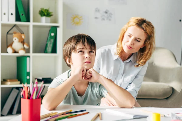 Dreamy kid with dyslexia looking up and child psychologist looking at him — Stock Photo