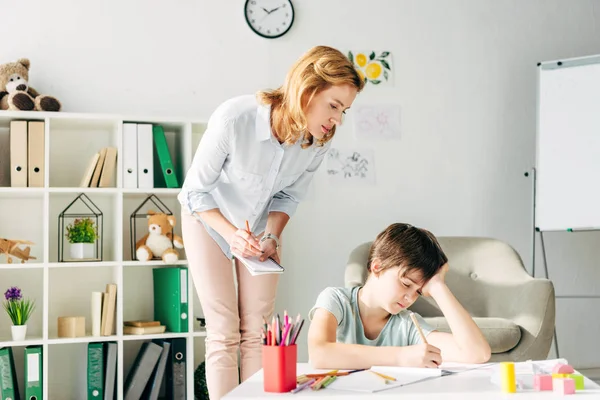 Bambino con dislessia disegno con matita e psicologo infantile guardandolo — Foto stock