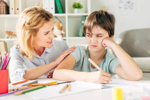 Sad kid with dyslexia holding pencil and smiling child psychologist talking to him — Stock Photo