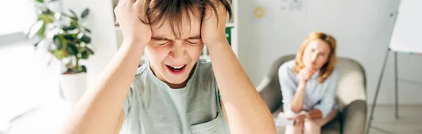 Panoramic shot of irritated kid with dyslexia shouting and holding head — Stock Photo
