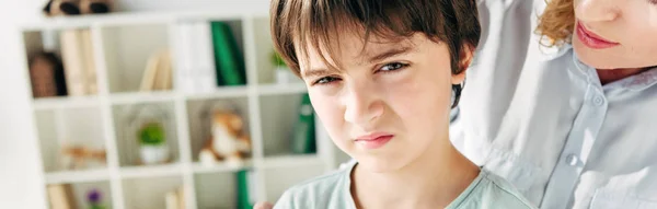 Plano panorámico de niño con dislexia mirando a la cámara y psicólogo infantil hablando con él - foto de stock