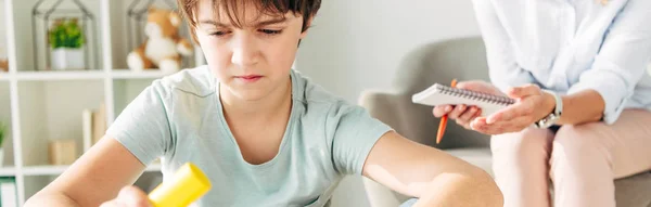 Panoramic shot of kid with dyslexia playing with building block and sitting at table — Stock Photo