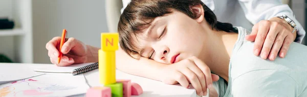 Panoramic shot of child psychologist hugging kid with dyslexia sleeping on table — Stock Photo