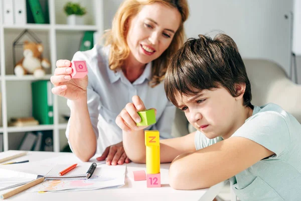 Bambino con dislessia e sorridente psicologo infantile che gioca con i mattoni — Foto stock