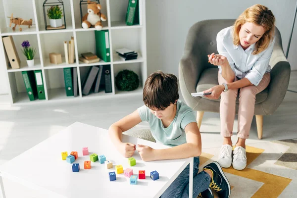 High angle view of irritated kid with dyslexia playing building blocks and child psychologist looking at it — Stock Photo