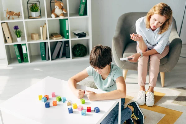 Visão de alto ângulo da criança irritada com dislexia jogando blocos de construção e psicólogo infantil olhando para ele — Fotografia de Stock