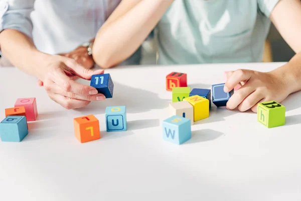 Обрезанный взгляд детского психолога и ребенка с дислексией, играющего со строительными блоками — стоковое фото