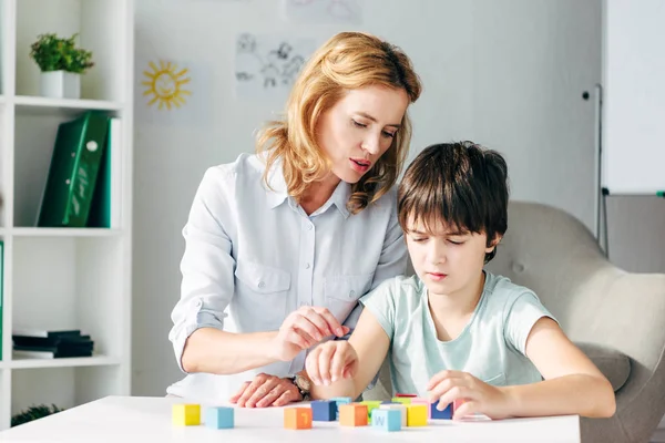 Psicólogo infantil y niño con dislexia jugando con bloques de construcción - foto de stock