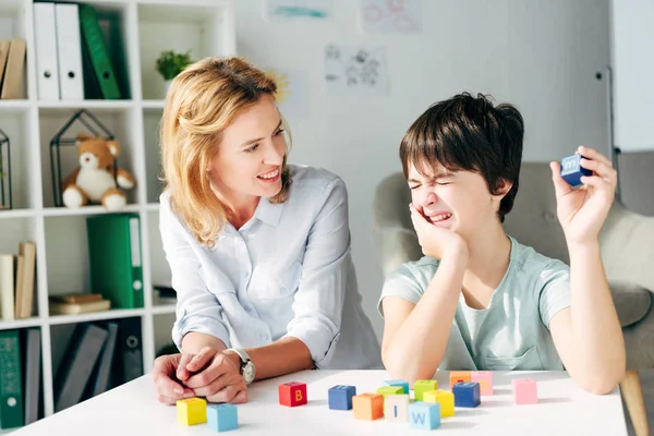 Psicologo infantile sorridente e bambino con dislessia che gioca con i mattoni — Foto stock