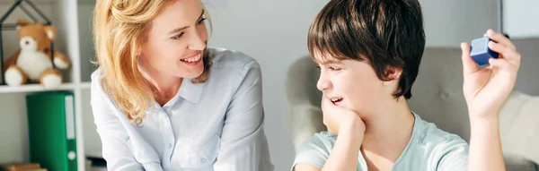 Plano panorámico de un psicólogo infantil sonriente mirando a un niño con dislexia - foto de stock