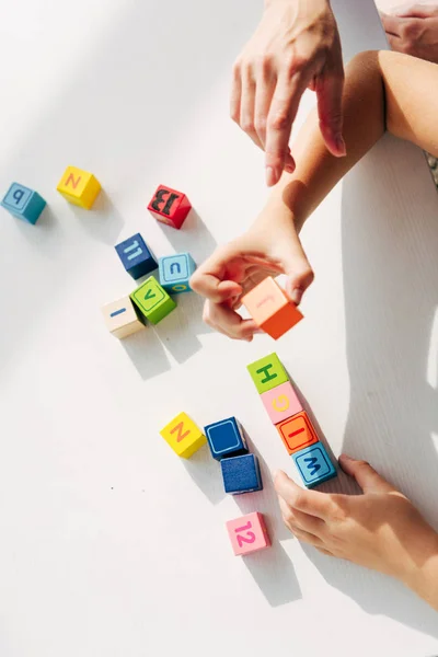Обрезанный взгляд детского психолога и ребенка с дислексией, играющего со строительными блоками — стоковое фото