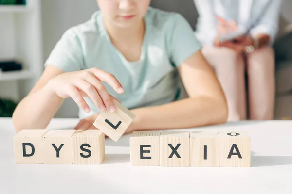 Vista recortada de niño con dislexia sentado en la mesa y jugando con cubos de madera - foto de stock