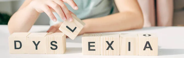 Panoramic shot of kid with dyslexia sitting at table and playing with wooden cubes — Stock Photo