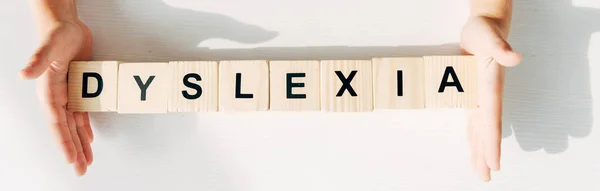 Panoramic shot of kid with dyslexia holding wooden cubes with lettering — Stock Photo