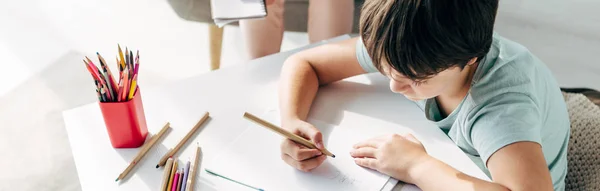 Panoramic shot of kid with dyslexia drawing on paper with pencil — Stock Photo