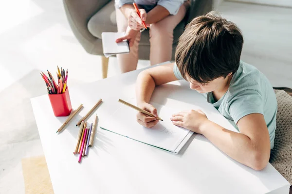 Vista de ángulo alto del niño con dislexia dibujo sobre papel con lápiz - foto de stock