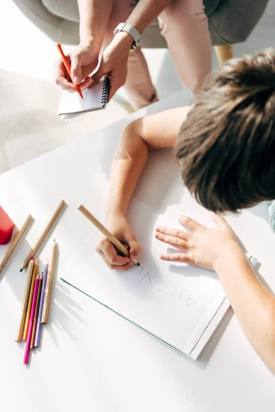 Vista recortada de niño con dislexia dibujo sobre papel con lápiz - foto de stock