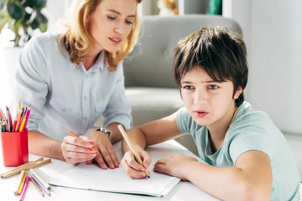 Criança com dislexia e psicólogo infantil sentado à mesa e segurando lápis — Fotografia de Stock