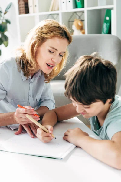 Ребенок с дислексией и детский психолог рисует карандашами — стоковое фото