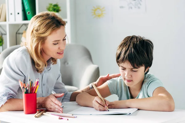 Kid with dyslexia drawing with pencil and child psychologist looking at it — Stock Photo