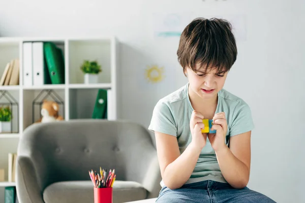 Bambino irritato con dislessia tenendo blocchi di legno e guardandolo — Foto stock