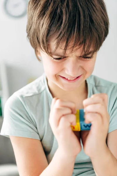 Irritated kid with dyslexia holding wooden building blocks and looking at it — Stock Photo