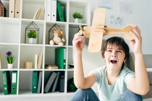 Cute kid with dyslexia yawning and playing with wooden plane — Stock Photo