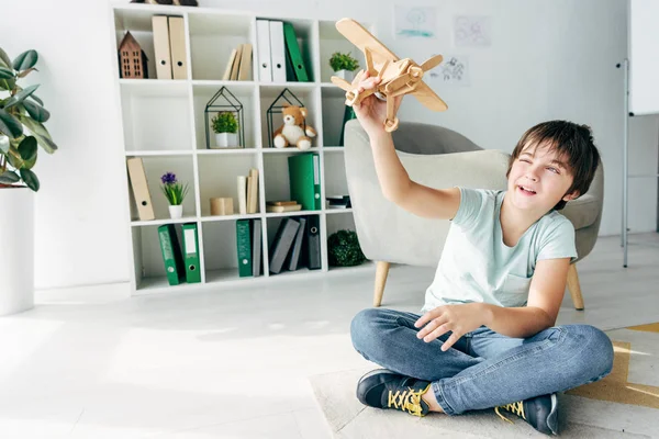 Милый ребенок с дислексией сидит на полу и играет с деревянным самолетом — стоковое фото