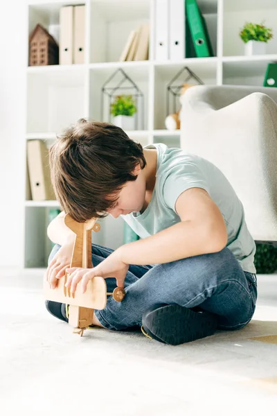 Kind mit Legasthenie sitzt auf dem Boden und hält Holzflugzeug — Stockfoto