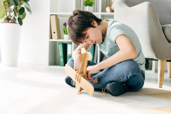 Enfant avec dyslexie assis sur le sol et tenant avion en bois — Photo de stock