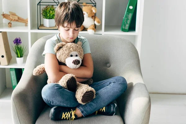 Criança com dislexia segurando ursinho de pelúcia e sentado em poltrona — Fotografia de Stock