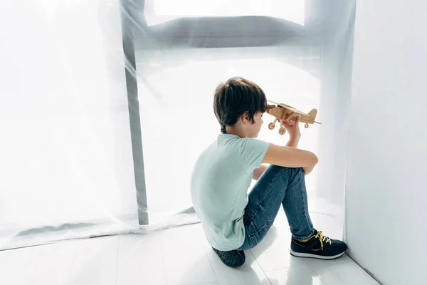 Visão de alto ângulo da criança com dislexia sentado no chão e brincando com o avião de madeira — Fotografia de Stock