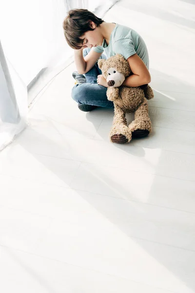 Vista ad alto angolo del bambino con dislessia seduto sul pavimento con orsacchiotto — Foto stock