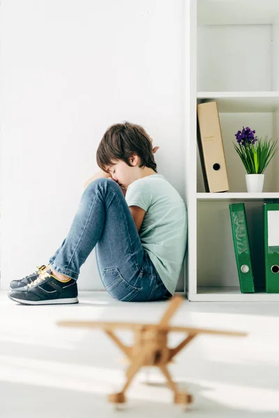 Selective focus of sad kid with dyslexia sitting on floor — Stock Photo