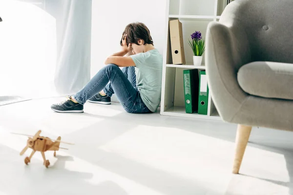 Seitenansicht eines traurigen Kindes mit Legasthenie auf dem Boden sitzend — Stockfoto