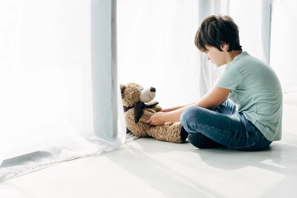 Enfant avec dyslexie assis sur le sol et regardant ours en peluche — Photo de stock