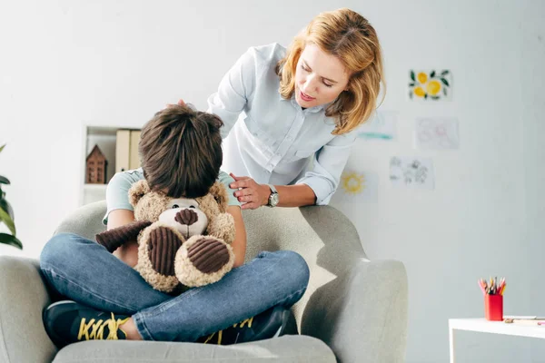 Triste enfant avec dyslexie tenant ours en peluche et psychologue enfant le calmer — Photo de stock